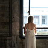 Back view of model wearing Aisling long organic cotton dress, highlighting low-back design and natural drape. Cream