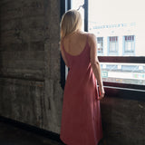 Back view of model wearing Aisling long organic cotton dress, highlighting low-back design and natural drape. Rubia
