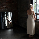 Back/side view of model wearing Aisling long organic cotton dress, highlighting low-back design and natural drape. Cream