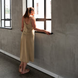Back/side view of model wearing Aisling long organic cotton dress, highlighting low-back design and natural drape. Pomegranate