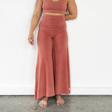 Front view of model wearing Danu organic cotton wide-leg flare pants, highlighting flattering seams and adjustable waistband, waistband unfloded. Naturally dyed with Rubia for sensitive skin