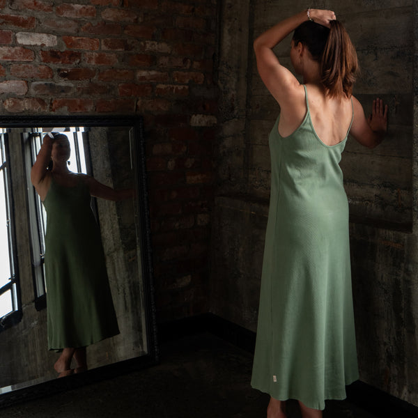 Back view of model wearing Aisling long organic ribbed cotton dress, highlighting low-back design and natural drape. Naturally dyed in Mulberry Green for sensitive skin 