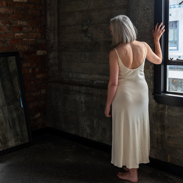 Back view of model wearing Aisling long organic rib cotton dress, highlighting low-back design and natural drape. Undyed for sensitive skin