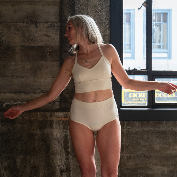 Front view of model wearing Branna organic cotton razorback bra, showing soft, supportive fit and wider strap. Natural cream for sensitive skin. Paired with Molly full briefs